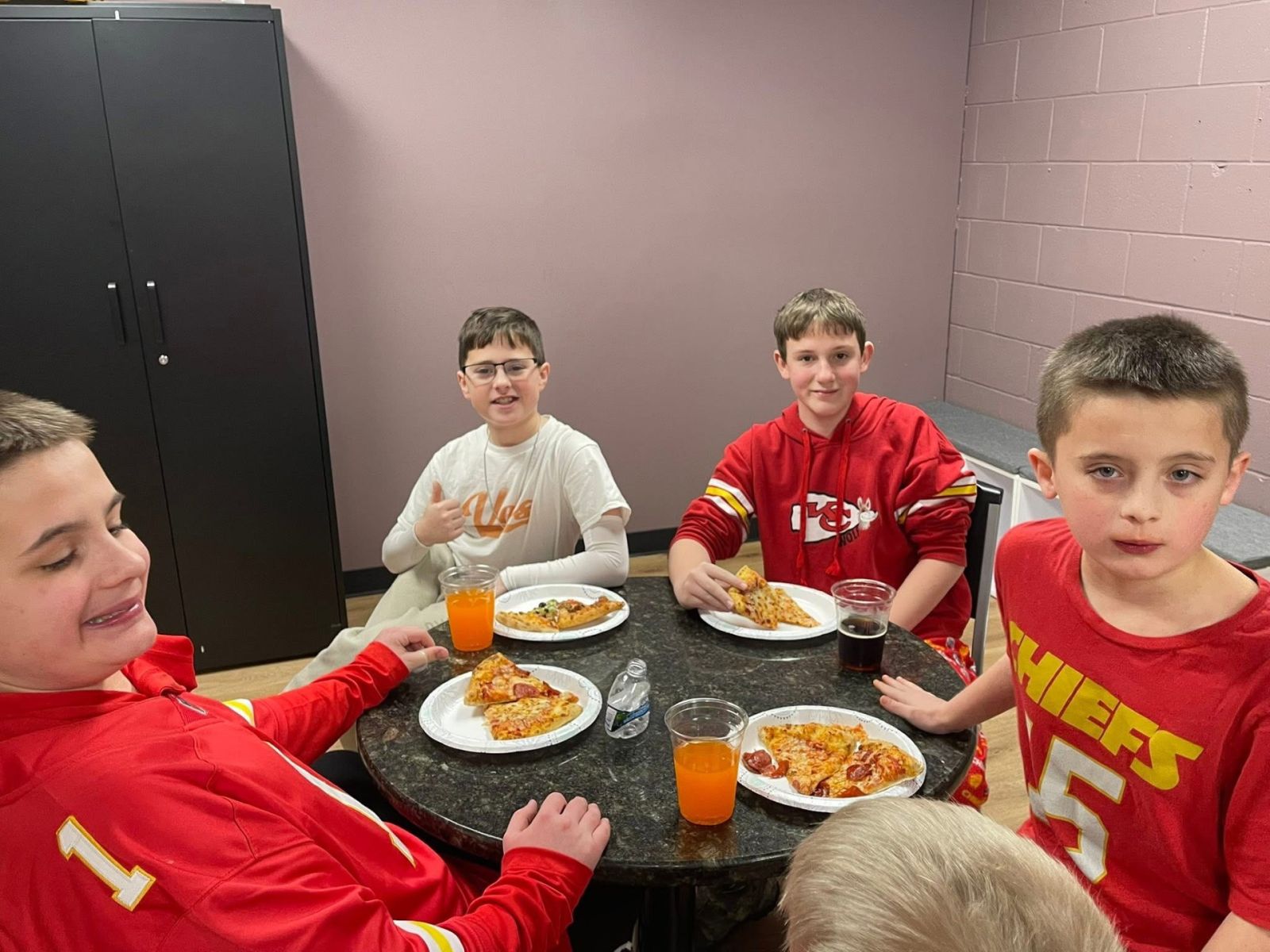 Participants in Kansas City Chiefs shirts sharing pizza around a table at a program social